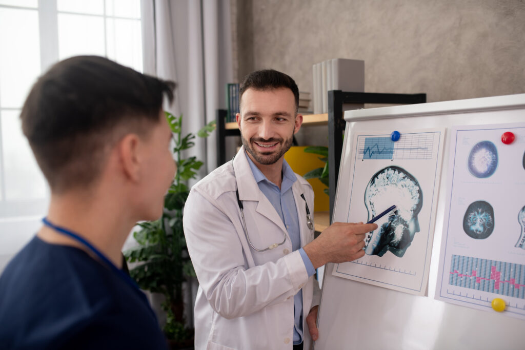 Médico neurologista sorrindo aponta para uma imagem de ressonância magnética do cérebro em um quadro branco, explicando o diagnóstico neurológico a um colega.