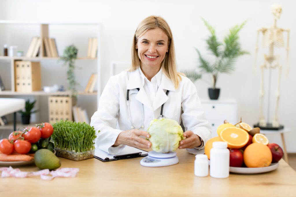 Nutricionista sorridente em seu consultório, pesando um repolho em uma balança, demonstrando a importância do plano alimentar personalizado na melhor dieta para emagrecer.