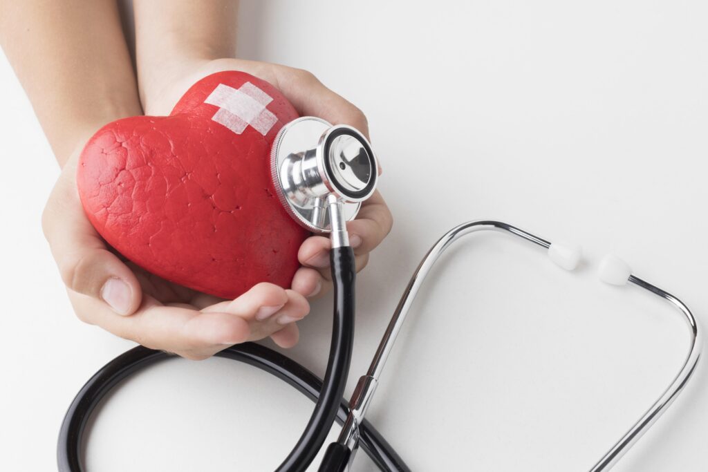 Mãos segurando um coração vermelho com um curativo, simbolizando a prevenção, o cuidado e a recuperação da saúde do coração para evitar um infarto silencioso.